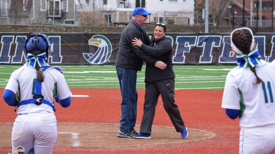 Dr. Michael Brady, administration of justice professor at Salve Regina University, and Jannelle Iaquinto, head softball coach for the Seahawks, embrace after Brady's ceremonial first pitch at a Toppa Field game in 2018, flanked by Salve Regina catcher Holly Kathios (left) and outfielder Lindsey Florent (right).